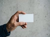 Male hand holding blank white business card against concrete wall background for corporate branding and contact information display.