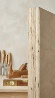 Close-up of plywood edge showing natural wood grain layers and texture in carpentry workshop with traditional woodworking tools in background.