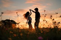 Romantic couple dancing in wildflower meadow at golden sunset, silhouetted against warm sky creating intimate moment in nature for love and relationship concepts.