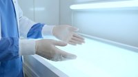 Young female healthcare professional wearing blue medical coat and white latex gloves working with laboratory biosafety cabinet in sterile clinical environment for medical research and diagnostics.