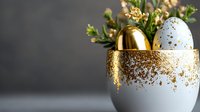 Decorative Easter eggs in white ceramic holder with gold glitter detail and spring flowers. Golden and speckled blue eggs create elegant holiday composition.