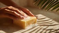 Hands washing with natural soap bar in warm sunlight with palm leaf shadow creating tropical spa atmosphere.