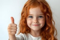 Young girl with bright red curly hair and blue eyes showing thumbs up gesture while smiling cheerfully against white background. Positive childhood expression.