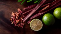 Fresh rhubarb stalks cut into pieces with bright green limes on dark wooden background, top view composition for cooking and baking preparation.