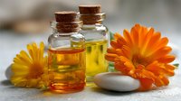 Natural calendula essential oil in glass bottles with cork stoppers and fresh orange marigold flowers for aromatherapy and skincare treatments.