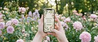 Hands holding smartphone with floral subscribe screen in blooming pink peony garden, social media content creation outdoors in summer nature setting.