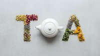 Word TEA spelled with colorful dried herbs and flowers on gray background, white ceramic teapot as letter E, flat lay composition.