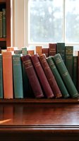 Vintage classic books arranged on wooden shelf near window with natural light creating warm cozy reading atmosphere for home library interior design.
