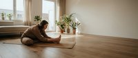 Young woman practicing yoga meditation on mat in bright modern living room with wooden floors and natural light streaming through windows.