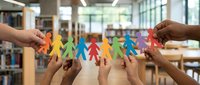 Diverse group of hands holding colorful paper cutout figures together in library setting, representing unity, teamwork, community support, and collaborative diversity in educational environment.