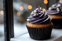 Chocolate cupcake with purple frosting swirl and pearl decorations in cozy bakery setting with warm bokeh lights for dessert and celebration themes.