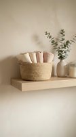 Woven jute basket with folded cotton towels on wooden shelf with eucalyptus branch in ceramic vase, minimalist bathroom organization and spa decor.