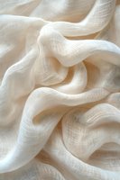 Soft white fabric with gentle folds and waves creates elegant texture. Natural light emphasizes delicate weave pattern and flowing curves of lightweight cloth material.