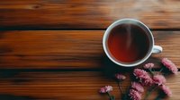 Overhead view of steaming black tea in white ceramic cup with delicate pink carnation flowers on rustic wooden table background, creating cozy atmosphere.
