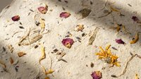 Handmade paper texture with dried flower petals and natural fibers creating organic botanical surface for crafting and artistic projects.