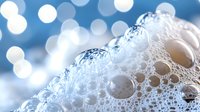 Close-up of soap bubbles and foam with sparkling water droplets against soft blue bokeh background for cleaning and hygiene concepts.