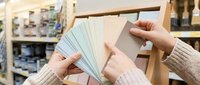 Woman hands selecting paint color samples from display rack in home improvement store for interior design renovation project.
