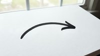 Simple black curved arrow pointing right drawn on white paper sheet lying on desk surface near window with natural daylight for business presentations.