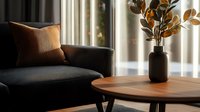 Minimalist living room interior with dark sofa, terracotta cushion, round wooden coffee table and decorative vase with dried leaves in moody lighting.