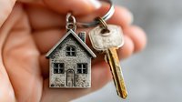 Hand holding house-shaped keychain with brass key symbolizing homeownership, real estate purchase, property investment, and new home keys.
