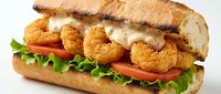 Crispy breaded shrimp sandwich with fresh lettuce and tomato on artisan bread with creamy sauce for restaurant menu and food advertising.