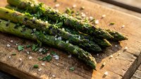 Fresh green asparagus spears with water droplets on rustic wooden cutting board, ready for cooking and meal preparation in kitchen.