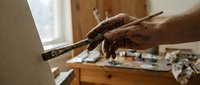 Artist hand holding paintbrush in creative studio workspace with easel and art supplies for painting and drawing projects.