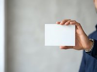 Man holding blank white card in hand against neutral gray wall background for business messaging and branding purposes.