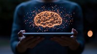 Glowing orange brain hologram floating above digital tablet held by person in dark environment, representing artificial intelligence and neural networks.