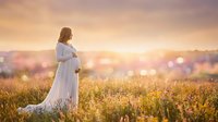 Pregnant woman in white dress standing in golden field at sunset, maternity photography concept for expecting mothers and family portraits.