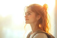 Young Asian woman with messy bun hairstyle smiling in warm golden sunlight, side profile view against bright backlit background showing natural happiness and joy.