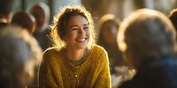 Young woman with radiant smile wearing yellow sweater in crowded cafe, illuminated by warm sunlight creating golden glow around her.