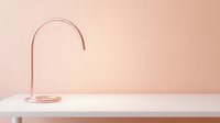 Minimalist rose gold curved lamp on white table against soft pink background, modern interior design element for contemporary home decor.