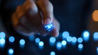 Magical glowing blue butterfly held between fingers against blurred bokeh lights background, creating ethereal atmosphere and dreamy mood.