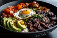 Korean beef bowl with sunny side up egg, sliced avocado, cherry tomatoes and steamed rice garnished with fresh herbs and sesame seeds served in black bowl.