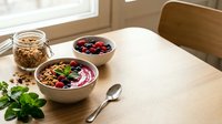 Healthy breakfast smoothie bowl with fresh berries, granola and mint on wooden table near window. Nutritious morning meal for wellness lifestyle.