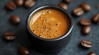 Fresh espresso with golden crema in black ceramic cup surrounded by roasted coffee beans on dark background, macro food photography.