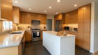 Modern kitchen interior with warm wood cabinets, white island and stainless steel appliances in contemporary home design for renovation inspiration.
