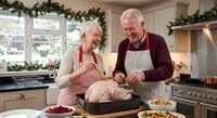 Senior Caucasian couple preparing Christmas turkey together in festive kitchen decorated with garland, sharing joyful moment during holiday cooking.