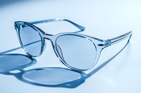 Transparent crystal eyeglasses frame casting soft shadow on blue background, modern minimalist optical accessory for vision correction and style.