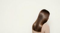 Woman with long, straight brown hair viewed from behind, wearing a neutral beige top against a white background. Isolated stock photo suitable for hair care, beauty, and wellness design projects.