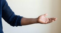 Male hand extended in open gesture wearing blue sweater sleeve against neutral background for presentation and offering concepts.