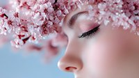 Young woman with closed eyes surrounded by delicate pink cherry blossoms in soft spring light creating dreamy beauty portrait for wellness and skincare concepts.