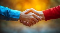 Close-up of firm handshake between two people wearing contrasting blue and red sleeves against warm blurred golden background symbolizing agreement and partnership.