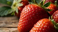 Fresh ripe strawberries with green leaves on rustic wooden surface, organic summer fruit harvest for healthy eating and natural food photography.