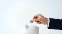 Hand in business suit inserting coin into white piggy bank on light background, symbolizing savings, investment, and financial planning.