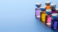 Colorful medical vials with aluminum caps arranged diagonally on blue background. Pharmaceutical glass containers filled with vibrant liquid medicines and vaccines.