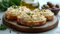 Creamy hummus spread on toasted bread slices garnished with fresh herbs and black pepper on wooden board. Healthy Mediterranean appetizer or snack.