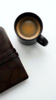 Black mug filled with fresh espresso coffee next to brown leather wallet on white background, overhead view for business and lifestyle concepts.