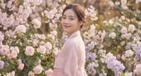 Young Asian woman in pink dress smiling among blooming cherry blossoms in spring garden for lifestyle and beauty content.